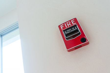 Bright red fire alarm box mounted on a white wall, designed for emergency situations, ensuring safety and quick notification in case of fire hazards.の写真素材