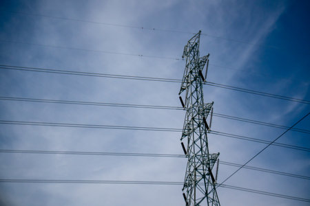 A tall metal power line tower stretches into a clear blue sky, showcasing modern energy infrastructure amidst a serene landscape. Ideal for technology themes.の写真素材