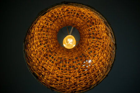 This unique woven light fixture features a warm glow with an elegant circular design, perfect for adding a cozy ambiance to any modern interior space.の写真素材
