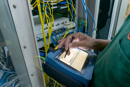 A technician uses a handheld device to manage and inspect network equipment. The scene shows colorful cables and connections in a busy tech environment.の写真素材