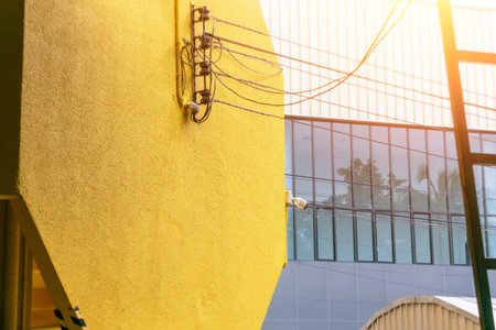 A vibrant yellow wall showcasing intricate electric wires creates a striking visual contrast with a contemporary building, highlighting urban design elements.の写真素材
