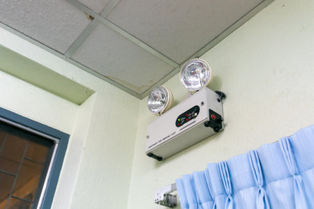 This image shows an emergency light fixture mounted on the ceiling, designed to provide illumination during power outages and emergencies.の写真素材