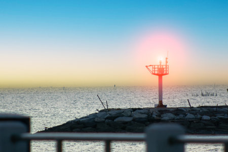 A serene lighthouse stands tall by the calm sea at sunset, offering a peaceful view of the horizon and showcasing the beauty of coastal landscapes.の写真素材