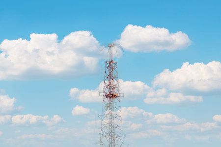 A striking red and white radio transmission tower punctuates a cloudy sky, symbolizing modern...