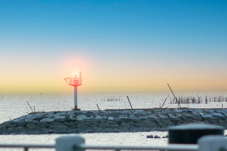 A serene sunset view over calm water featuring a lighthouse on a rocky outcrop, creating a peaceful coastal scene ideal for nature lovers and travelers.の写真素材