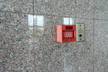 Close-up of a red fire alarm box mounted on a smooth granite wall. This device serves as an important safety feature for emergency response in buildings.の写真素材