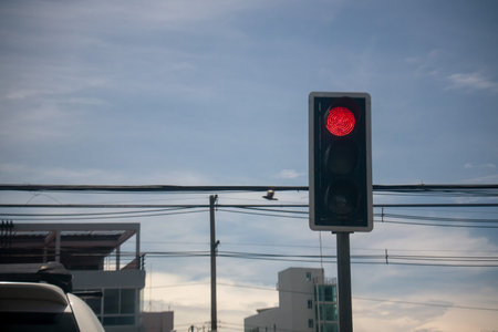 A red traffic light stands prominently against a clear blue sky, indicating a stop. Surrounding...