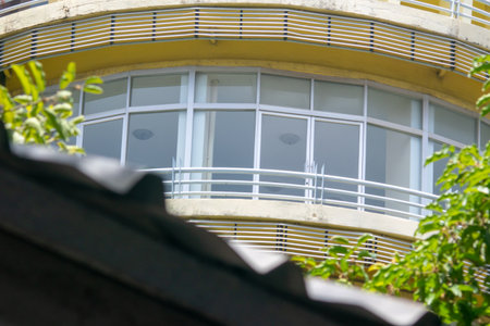 A captivating view of modern architecture featuring a curved design with large windows, surrounded by greenery, showcasing contemporary urban living aesthetics.の写真素材