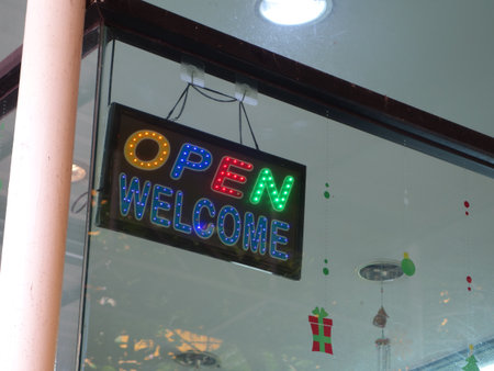 An inviting neon "Open" and "Welcome" sign hangs in a storefront, offering a cheerful atmosphere for customers. Ideal for business promotions.の写真素材