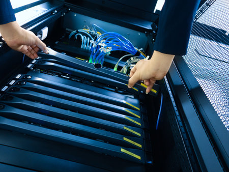 A technician performs maintenance on server equipment in a data center. The image shows hands...