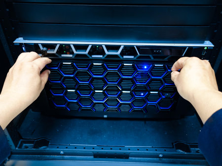 Hands adjusting a server within a data center rack, showcasing technology and IT infrastructure. The blue light indicates system status, emphasizing organization and maintenance.の写真素材
