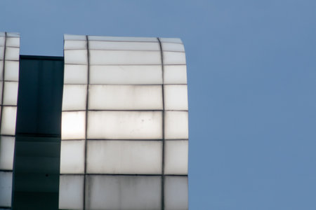 A close-up view of a modern architectural structure with unique wavy shapes and a glass facade against a clear blue sky, showcasing innovative design elements.の写真素材