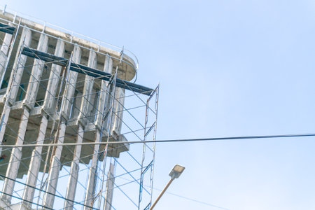 A detailed view of a construction site showing scaffolding supporting a building structure against a clear blue sky. The scene captures the essence of urban development.の写真素材
