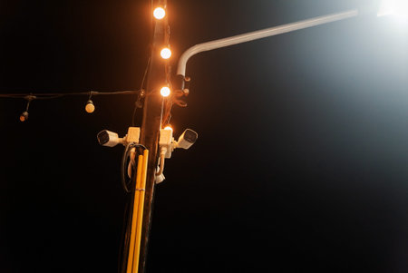 This image showcases a nighttime scene featuring security cameras mounted on a pole, illuminated by...