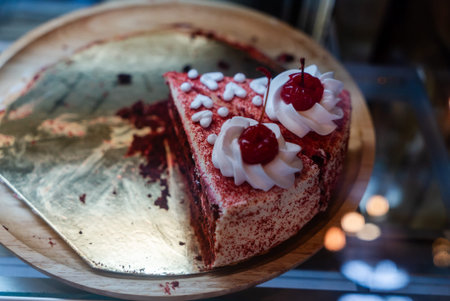 A tempting slice of red velvet cake topped with creamy frosting and cherries, perfect for any...