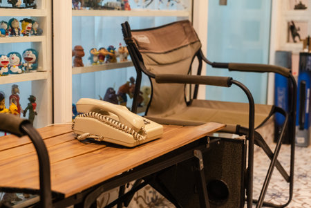 A vintage telephone rests on a rustic wooden table in a cozy interior space. The setting features comfortable seating and an artistic display of collectibles.の写真素材