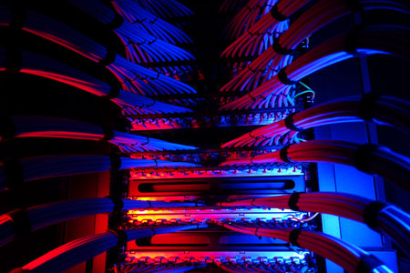 A vibrant view of a modern data center featuring illuminated cables in blue and red tones. The...