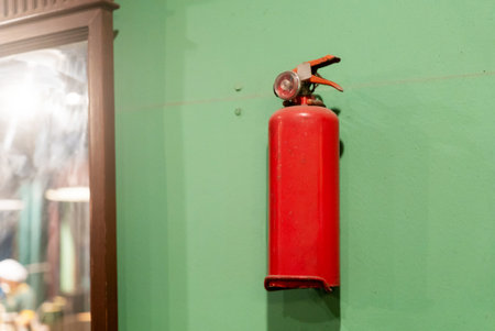 A vibrant red fire extinguisher mounted on a green wall, emphasizing fire safety in interior spaces. Ideal for use in educational materials and safety promotions.の写真素材