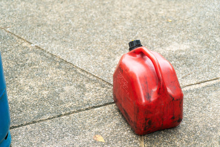 A bright red plastic gas can rests on a concrete surface, showcasing its durable design and utility for fuel storage and transportation needs.の写真素材