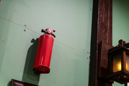 A bright red fire extinguisher is securely mounted on a green wall, serving as a crucial safety measure for fire emergencies in any setting.の写真素材