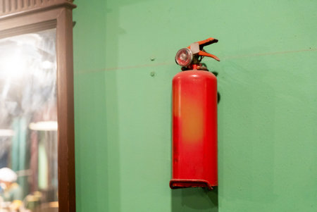 A vibrant red fire extinguisher mounted on a green wall, showcasing urban safety equipment. The design blends functionality with aesthetics to enhance any interior space.の写真素材