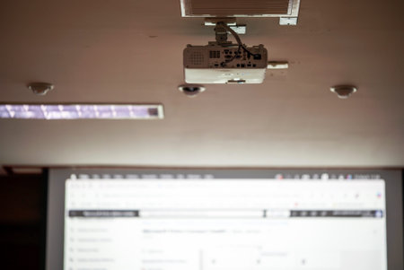 A ceiling-mounted projector illuminates a presentation screen in a modern conference room,...