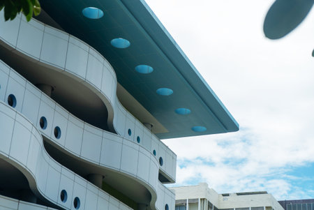 Modern architectural building showcases unique curved design with vibrant blue elements against a bright sky, emphasizing creativity and contemporary aesthetics.の写真素材