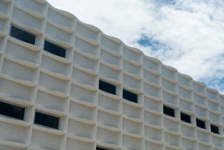 Captivating modern building facade showcasing an abstract design with unique geometric lines and patterns under a bright sky with clouds.の写真素材