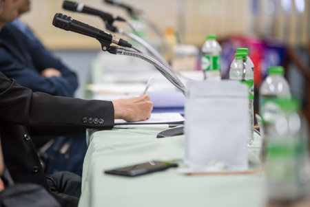 A professional meeting room featuring microphones and water bottles on a table during a discussion. Participants are engaged in collaboration to share ideas and strategies.の写真素材