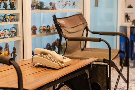 A nostalgic vintage phone rests on a wooden table beside a comfy chair, showcasing a cozy indoor...