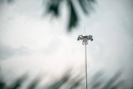 A solitary light pole stands against a cloudy sky, surrounded by soft foliage. The image captures urban lighting infrastructure in a serene setting.の写真素材