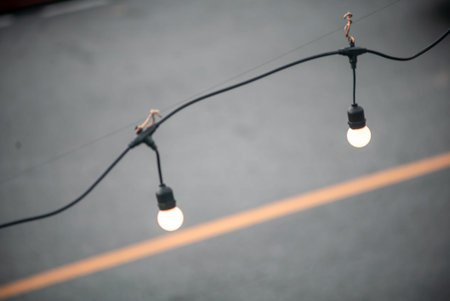 Two glowing bulbs hang from a wire, casting a warm light over a paved surface, creating a cozy...