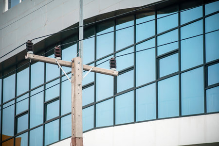 A close-up view of urban power lines contrasted against sleek glass architecture, highlighting the...