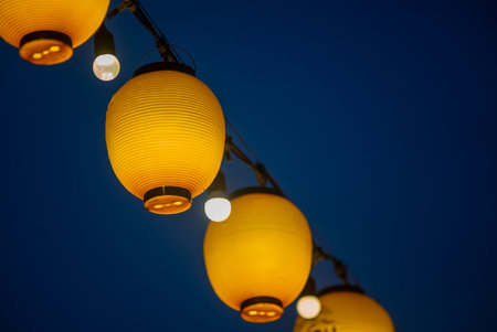 A vibrant display of yellow lanterns hanging against a deep blue night sky, creating a warm and...