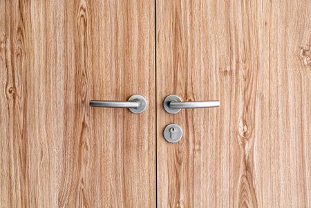 Close-up view of a modern wooden door featuring sleek metal handles. The natural wood grain provides...