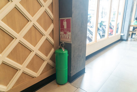 A green fire extinguisher positioned next to a safety sign in a modern indoor setting, emphasizing fire safety and emergency preparedness in public spaces.の写真素材