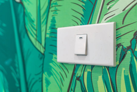 A close-up of a white light switch on a vibrant green leaf-patterned wall, showcasing modern design...