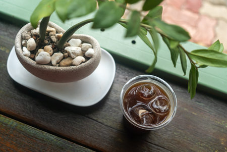A serene scene featuring a glass of iced tea beside a potted plant with smooth stones. This tranquil...
