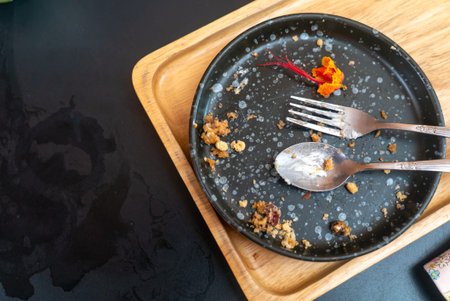 An empty plate with utensils shows remnants of a meal, featuring crumbs and an orange flower garnish. The scene captures the essence of dining.