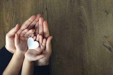 White paper heart in child's and female palms, top view. Love, Mother's day, family concept.の写真素材