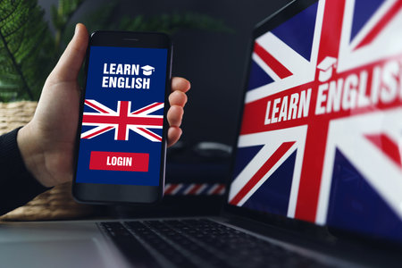 Learning foreign languages online. Woman holding smartphone with app for studying English on screen, copy space. Laptop with British flag in back.の写真素材