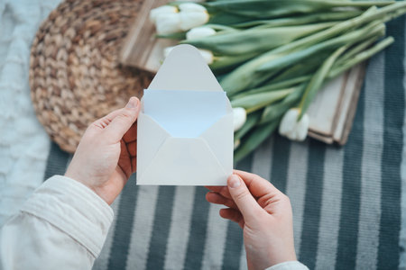 Hands with an empty envelope on a background of flowers, a place for your text.