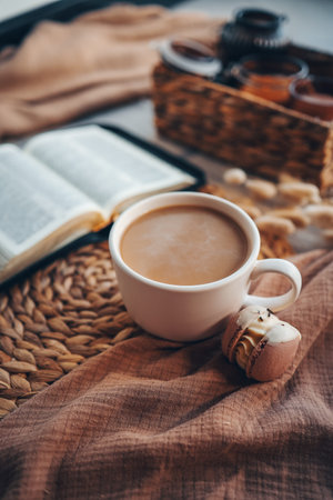 Cup of coffee and macarons, open book in cozy home interior, good morning concept.