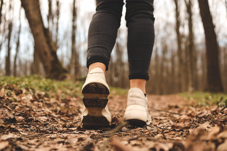 Close up of a womans legs running in the forest. Sports shoes. Trees and leaves in background....
