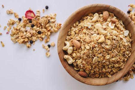 Granola with nuts and almonds on a white background, cereal scattered around.