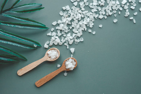 Sea salt on a green background in wooden spoons top view.の写真素材