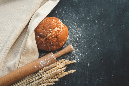 Homemade fresh bread, ears of wheat and a rolling pin on a black background, flat lay top view.