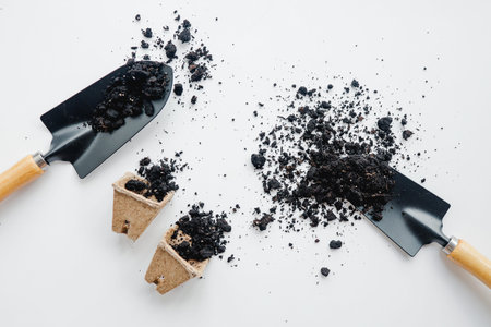 Gardening tools with soil and cardboard pots on white background.