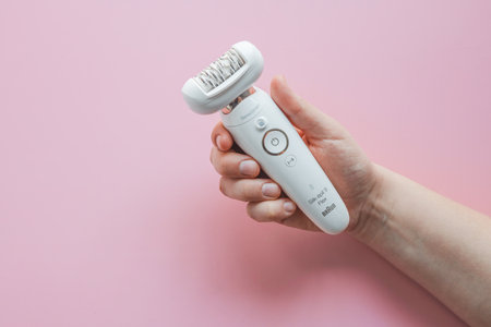 Woman holding a stylish epilator in her hand on a pink background.の写真素材