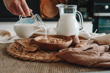 Milk jug pouring milk into the bowl with natural muesli made from mix of unprocessed whole grains.